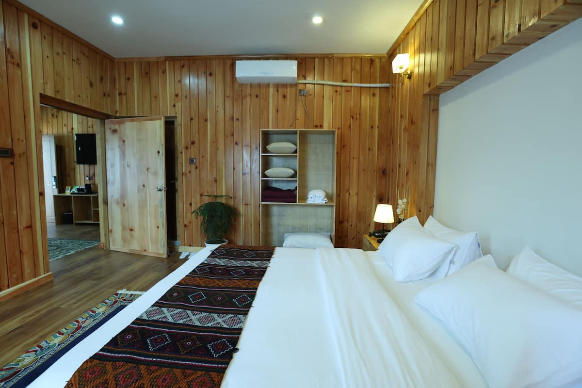 A wooden-paneled room with a bed, a mirror, a shelf with pillows, a plant, and a lamp.