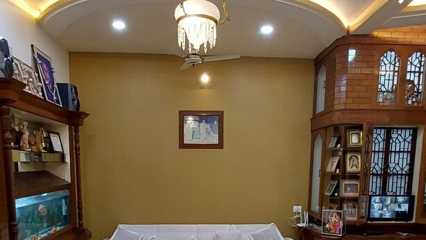A modern living room with a sectional sofa, a chandelier, a fish tank, and a wooden cabinet with framed pictures. - KAPOOR SAHAB HOMESTAY it's a home away from home (Varanasi)