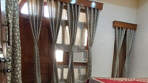 A room with a marble floor, a bed with a red bedspread, wooden furniture, and patterned curtains. - KAPOOR SAHAB HOMESTAY it's a home away from home (Varanasi)