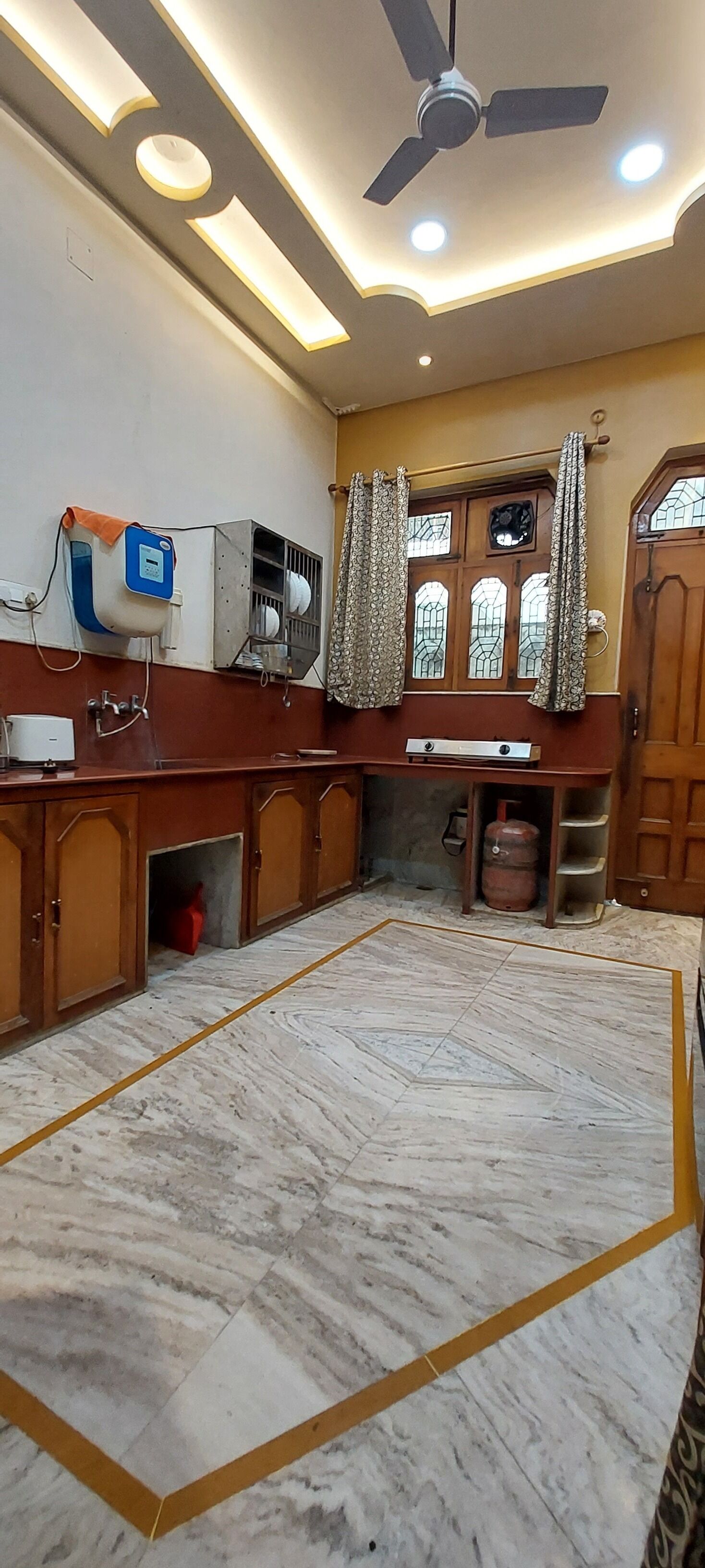 Habitació amb sòl de marbre, ventilador al sostre, finestra amb cortines i porta de fusta.