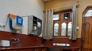 Habitació amb sòl de marbre, ventilador al sostre, finestra amb cortines i porta de fusta.