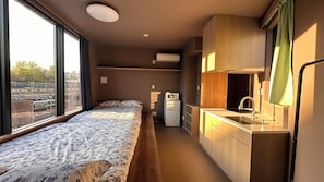 Una habitación pequeña con cama, una kitchenette compacta y ventana con vistas a un tren.