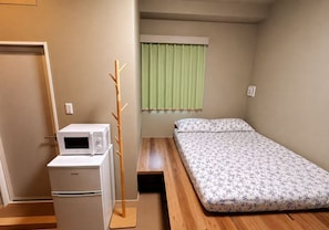 A compact room with a bed, a microwave, and a wooden coat rack. - WINN hotel (Tokyo)