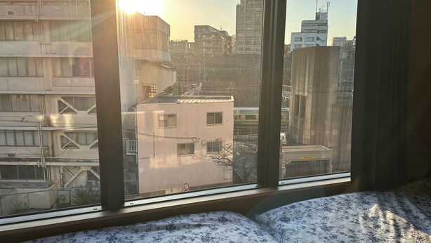 Vista da janela de um horizonte urbano com edifícios, placa de limite de velocidade de 40 km/h e uma cama com colcha florida.