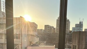 Quarto com uma grande janela com vista para a paisagem urbana ao pôr do sol.