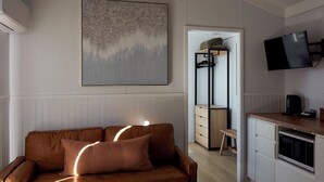 Una sala de estar moderna con un sofá de cuero marrón, un televisor montado y una zona de cocina con microondas.