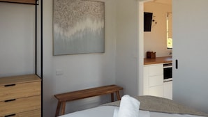 Un dormitorio con una cama, un banco de madera, un aparador y un cuadro en la pared.