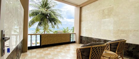 A room with a view of palm trees, a balcony with a bamboo screen, a fireplace, and wicker furniture.