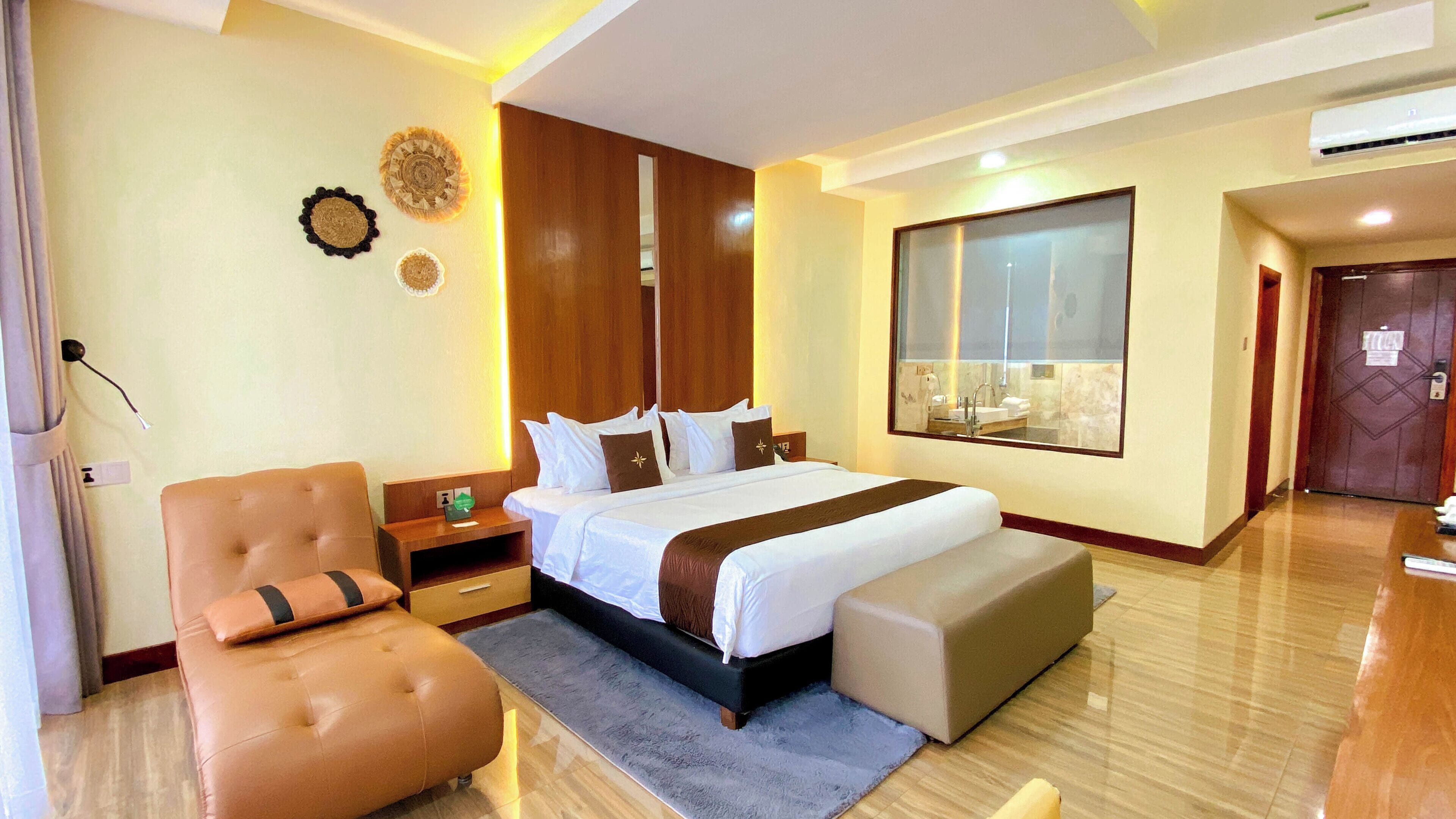 A hotel room with a large bed, a sitting area, a wardrobe, a mirror, and a view of the bathroom.