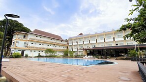 A hotel with a swimming pool, outdoor seating, and a covered area with umbrellas.