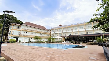 Un hotel con piscina, zona de estar al aire libre y área cubierta con sombrillas.