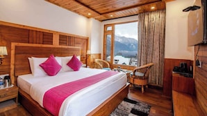 A wooden-framed bedroom with a large bed, two chairs, a TV, and a view of mountains. - Snow Creek By JNS Hotels CentrallyHeated (Manali)