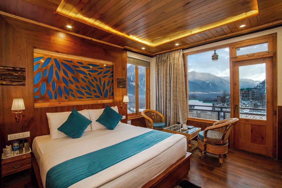 A hotel room with a large bed, a view of mountains, and a balcony with wicker furniture.