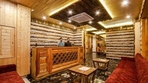 A lobby with a wooden reception desk, a red sofa, and a stone-tiled floor. - Snow Creek By JNS Hotels CentrallyHeated (Manali)
