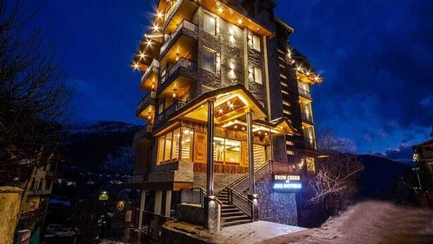 A multi-story hotel with a prominent staircase, balconies, and a sign indicating 'Snow Green' and 'Jr. Motel' on the ground floor. - Snow Creek By JNS Hotels CentrallyHeated (Manali)