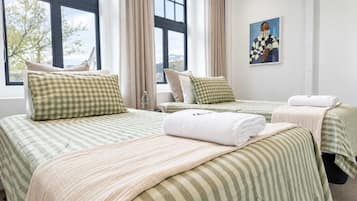 A hotel room with two beds, each with a striped bedspread and checkered pillows. There is a painting on the wall and a window with curtains.
