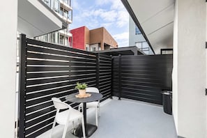 A modern outdoor seating area with a black fence, white chairs, and a round table with a potted plant.