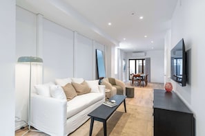 Ein modernes Wohnzimmer mit einem weißen Sofa, einem Couchtisch, einem an der Wand befestigten Fernseher und einem Essbereich im Hintergrund.