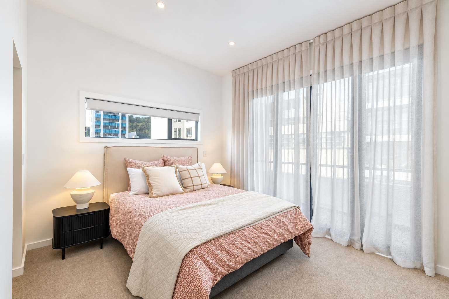 Un dormitorio con cama, lámparas de noche, una ventana con cortinas y un cuadro en la pared.