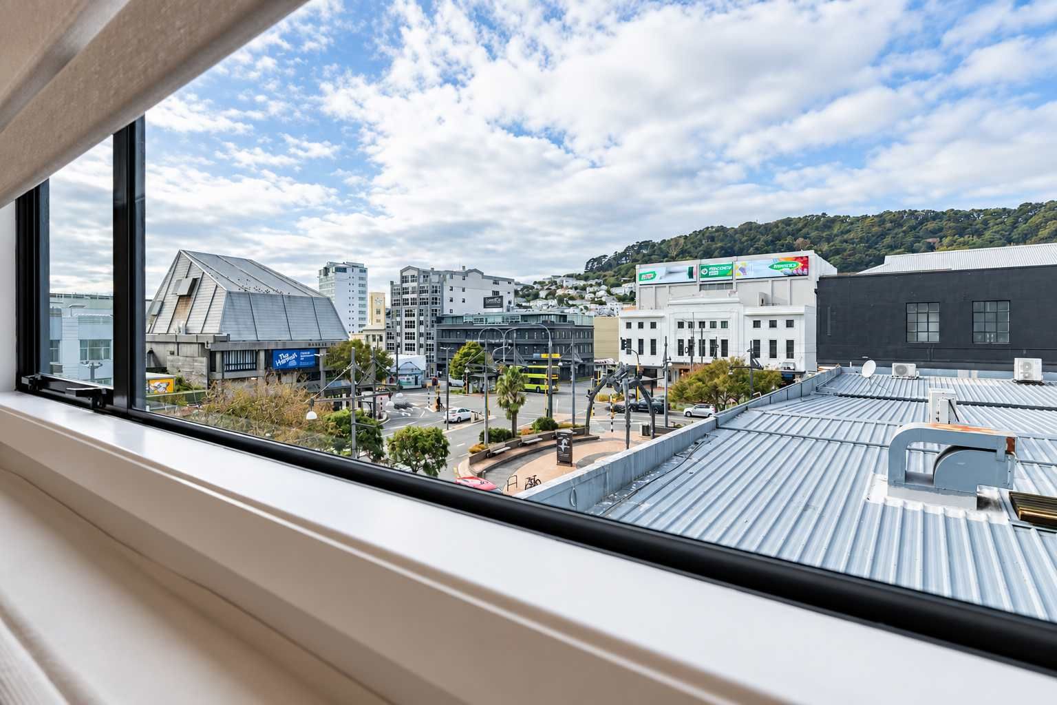 A view from a window overlooking a cityscape with buildings, a street, and a hill in the distance.
