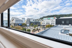 A view from a window overlooking a cityscape with buildings, a street, and a hill in the distance. - The Windsor | Wellington CBD | Stylish 3BR (Te Aro)