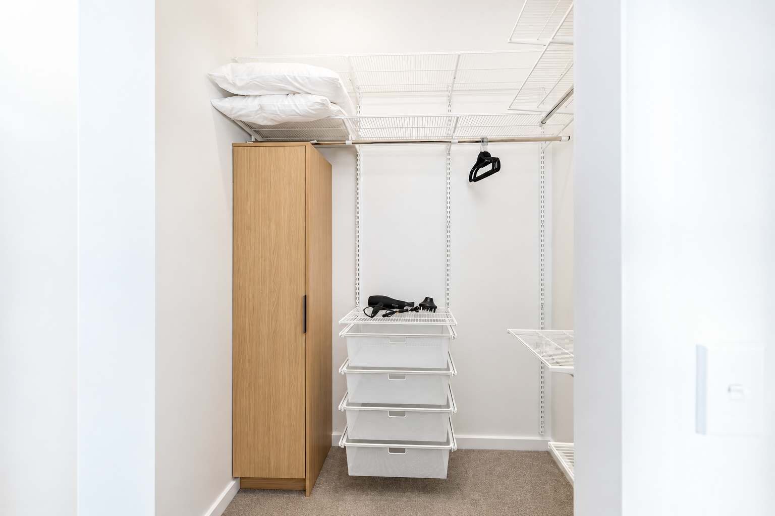 A walk-in closet with a wooden wardrobe, white storage bins, and a hanging organizer.