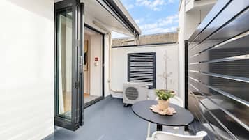 A small outdoor patio with a table and chairs, a potted plant, and a sliding glass door leading to an interior space.