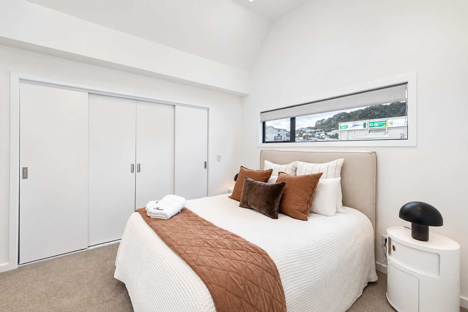 Un dormitorio con cama, mesita de noche, ventana con vistas y armario.