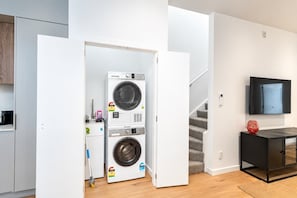 Ein Waschraum mit zwei gestapelten Waschmaschinen, einer Treppe, einem an der Wand montierten Fernseher und einem kleinen Schrank mit einer Dekoration.