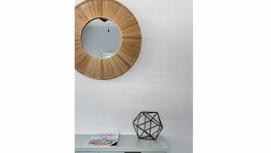 Pyöreä peili seinällä, vaaleansininen kaappi, jonka päällä on lehti ja geometrinen esine, sekä laatikko, jossa on kultainen vetokahva.