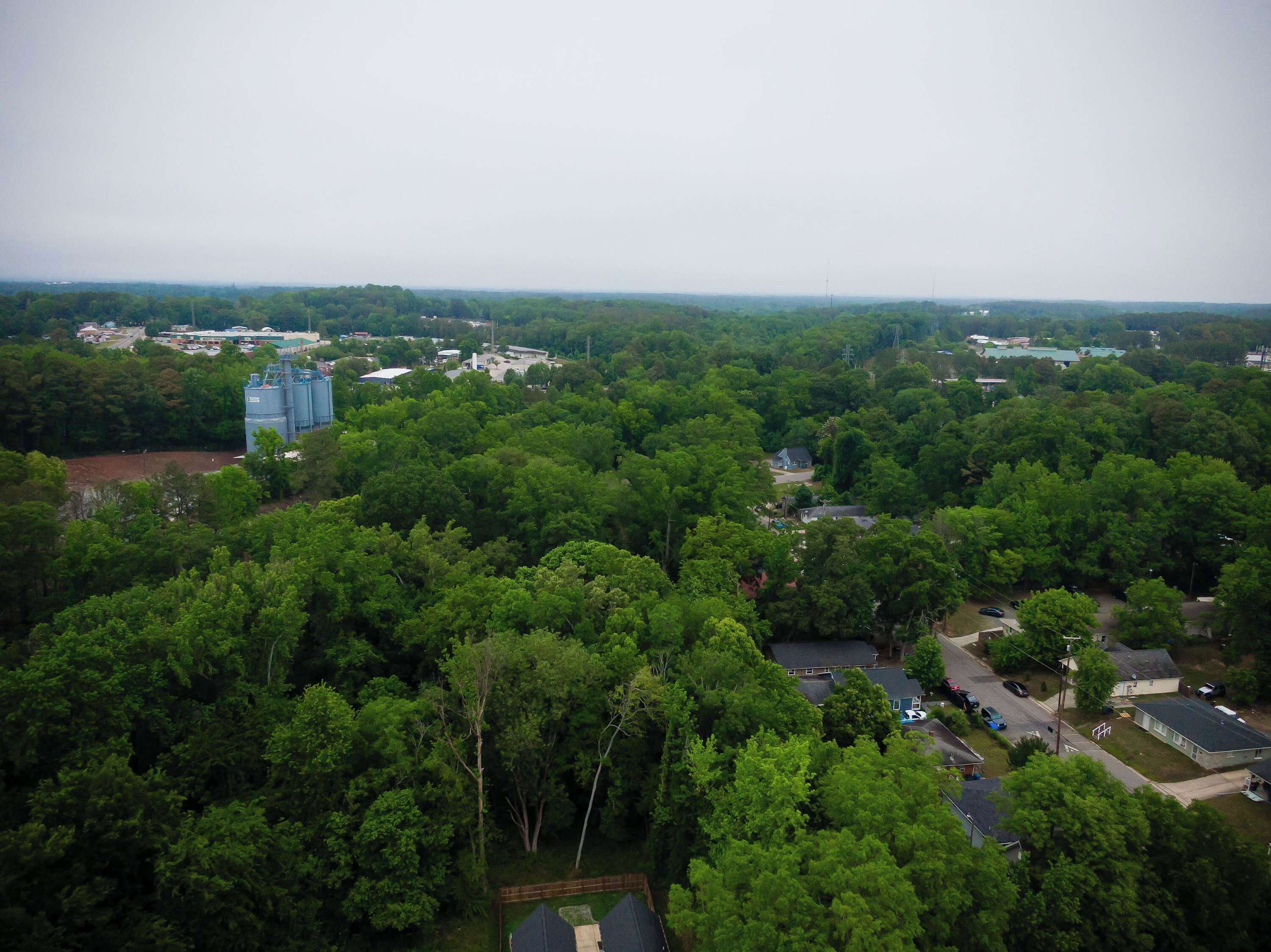 An aerial view of a residential area with dense greenery, a few houses, and industrial buildings.