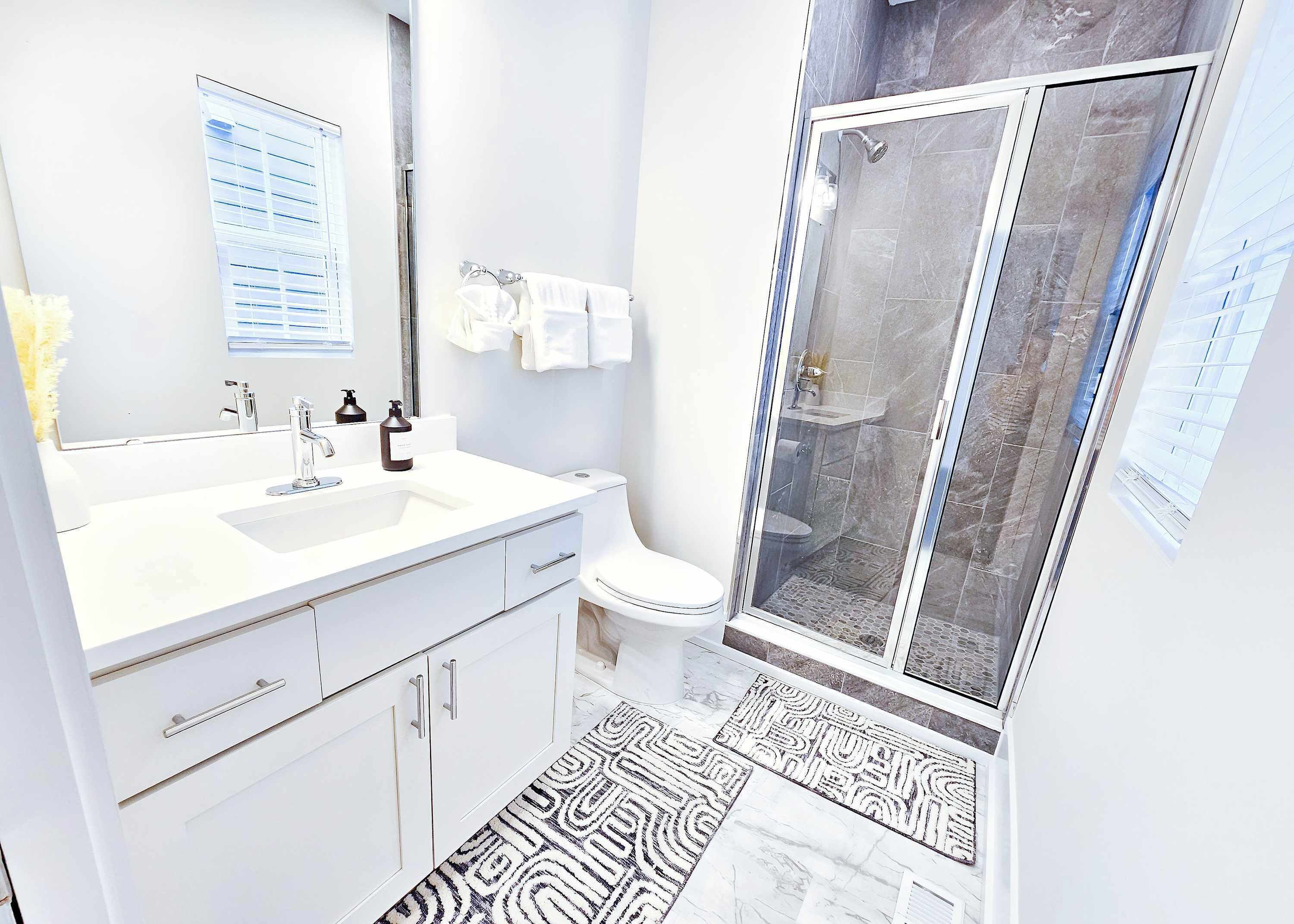 Une salle de bain moderne avec un grand miroir, un lavabo blanc et une douche à l’italienne.