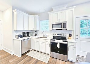 Eine moderne Küche mit weißen Schränken, einer Mikrowelle, einem Toaster, einer Kaffeemaschine und einem Backofen.