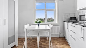 A kitchen with a white table and chairs, a window with a view, and a microwave. - Comfort Studio Leeds Ideal for Work Study Street Parking (Leeds)