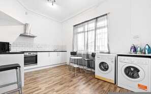 Cocina moderna con microondas, horno y lavadora. Hay dos sillas y una mesa.