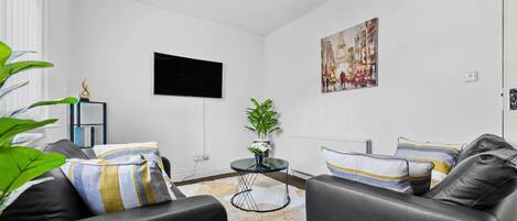 A modern living room with a black leather sofa, a round coffee table, and a flat-screen TV mounted on the wall.