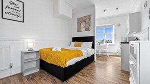 A modern bedroom with a black and white bed, a yellow throw, a bedside lamp, a framed quote, and a view to the kitchen. - Comfort Studio Leeds Ideal for Work Study Street Parking (Leeds)