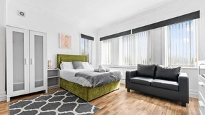 Um quarto moderno com cama verde, sofá cinza e tapete estampado.