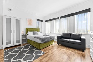 A modern bedroom with a green bed, a grey sofa, and a patterned rug. - Leeds City Studio Stay Ensuite Kitchenette Street Parking (Leeds)