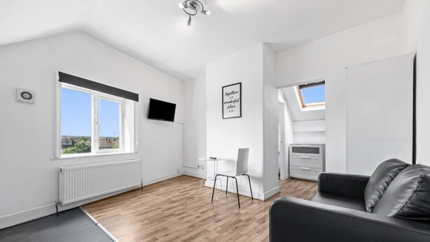 Un apartamento moderno con un ventanal grande, un televisor de pantalla plana, una mesita, un sofá y una kitchenette.