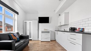 A modern kitchen with white cabinets, a black countertop, and a television mounted above the sink. - Modern Leeds Studio Retreat Sleeps 2 Street Parking (Leeds)