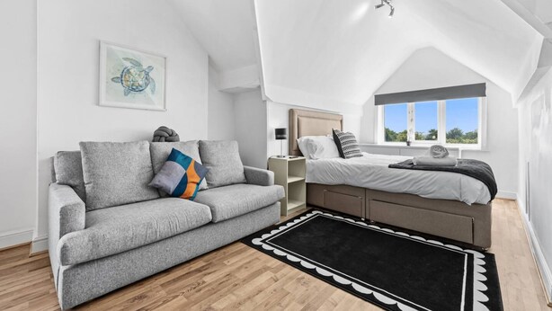 Un dormitorio estilo loft moderno con techo inclinado, un sofá gris, una cama con vistas y una obra de arte enmarcada en la pared.