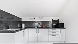 Una cocina moderna con encimera negra, armarios blancos, un hervidor, un microondas y un rollo de papel de cocina.