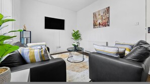 Una sala de estar moderna con un sofá de cuero negro, una mesita redonda y una planta en maceta.
