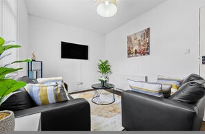 Ein modernes Wohnzimmer mit einem schwarzen Ledersofa, einem kleinen runden Tisch und einer Topfpflanze.