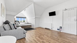Un dormitorio estilo loft moderno con techo inclinado, una cama grande, un sofá gris, un televisor de pantalla plana y una puerta blanca.