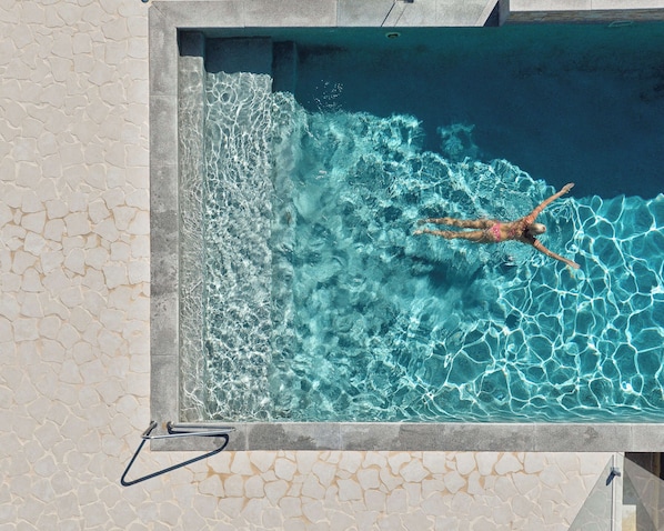 A rectangular swimming pool with clear water, a person swimming, and a stone wall surrounding the pool.