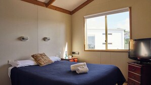 Ein Schlafzimmer mit Bett, Fernseher, Fenster und Kommode.