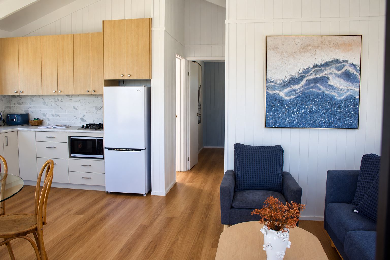 A modern kitchen with wooden cabinets, a white refrigerator, and a dining area with a glass table and chairs.