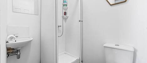 A bathroom with a shower, toilet, sink, and a mirror.